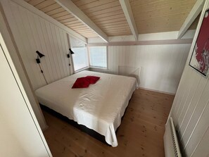 Een slaapkamer met een bed, een rood kussen, een raam met jaloezieën en een verwarming.