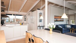 Una cocina moderna con armarios blancos, una isla central con sillas y una mesa de comedor. Hay un sofá azul y un cuadro en la pared.