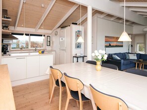 Ett modernt kök med vita skåp, en köksö med stolar och ett matbord. Det finns en blå soffa och en tavla på väggen.