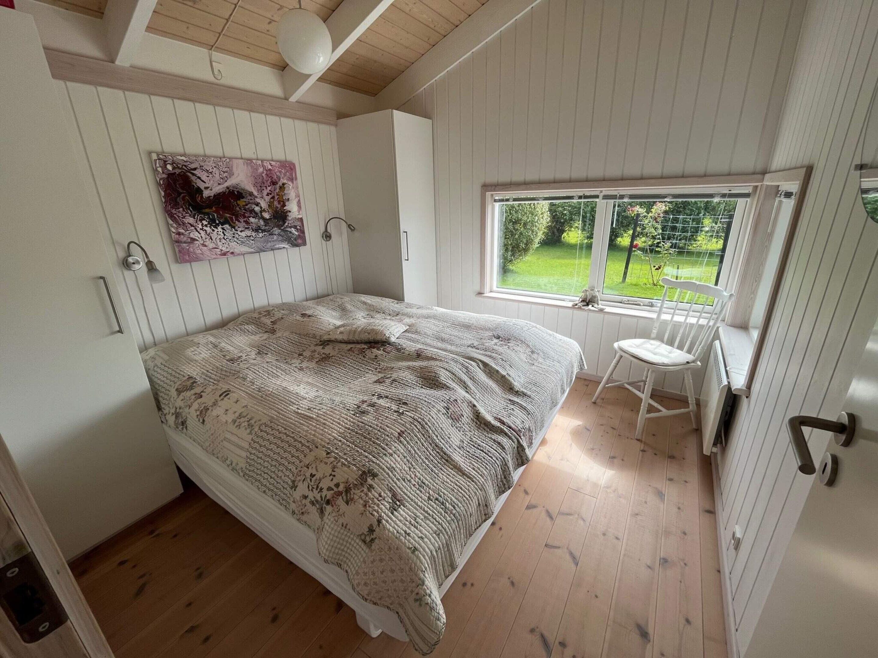 Une chambre avec un grand lit, une fenêtre donnant sur un paysage verdoyant et un tableau accroché au mur.
