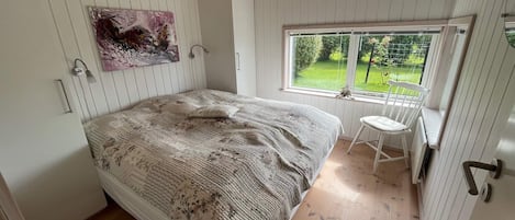 A bedroom with a large bed, a window with a view of greenery, and a painting on the wall.