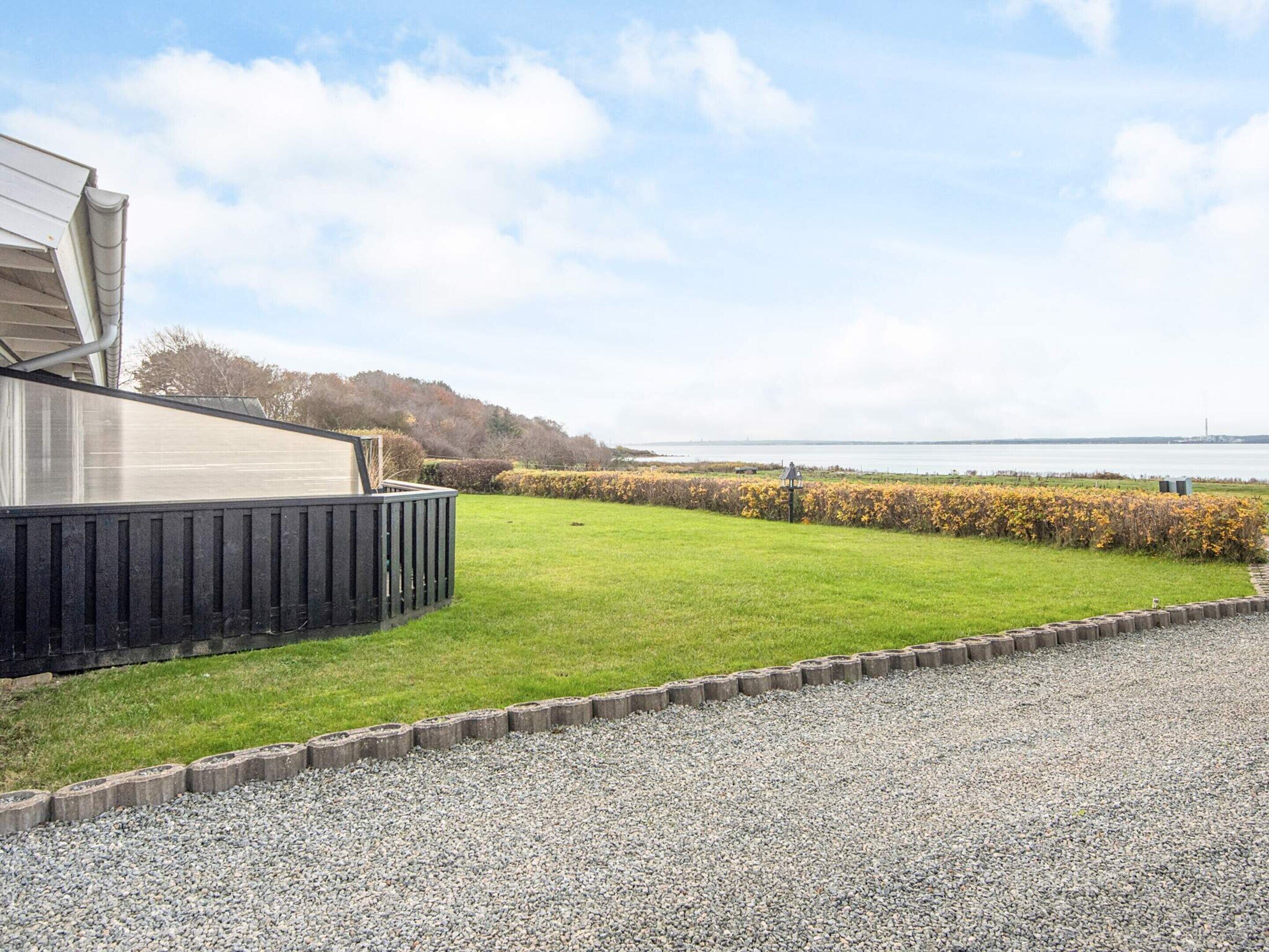 A view of a grassy area with a gravel path, a wooden fence, and a body of water in the background.