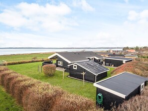 A coastal residential area with multiple black-roofed buildings, a grassy field, and a view of the sea. - 4 Star Holiday Home in Knebel (Knebel)