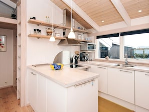 A modern kitchen with white cabinetry, wooden beams, and a large window. - 4 Star Holiday Home in Knebel (Knebel)