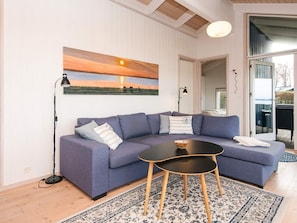 A modern living room with a sectional sofa, a small round table, and a large painting of a sunset. - 4 Star Holiday Home in Knebel (Knebel)
