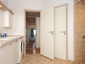 A compact kitchen with a washing machine, a sink, and a window with curtains. - 4 Star Holiday Home in Knebel (Knebel)