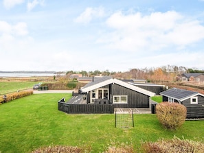 Ett modernt hus med en stor terrass, en inhägnad trädgård och utsikt över havet.