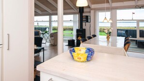 Un comedor amplio con una larga mesa y sillas, un gran ventanal con vistas al mar y una cocina moderna con una isla central.