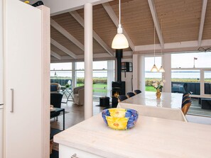 Ett rymligt matområde med ett långt bord och stolar, ett stort fönster med utsikt över havet och ett modernt kök med en central köksö.