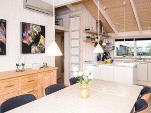 Eine moderne Küche mit weißen Schränken, einer Holz Arbeitsplatte und Pendelleuchten. Es gibt eine Essecke mit Tisch und Stühlen, und ein Blumenvasen auf dem Tisch.