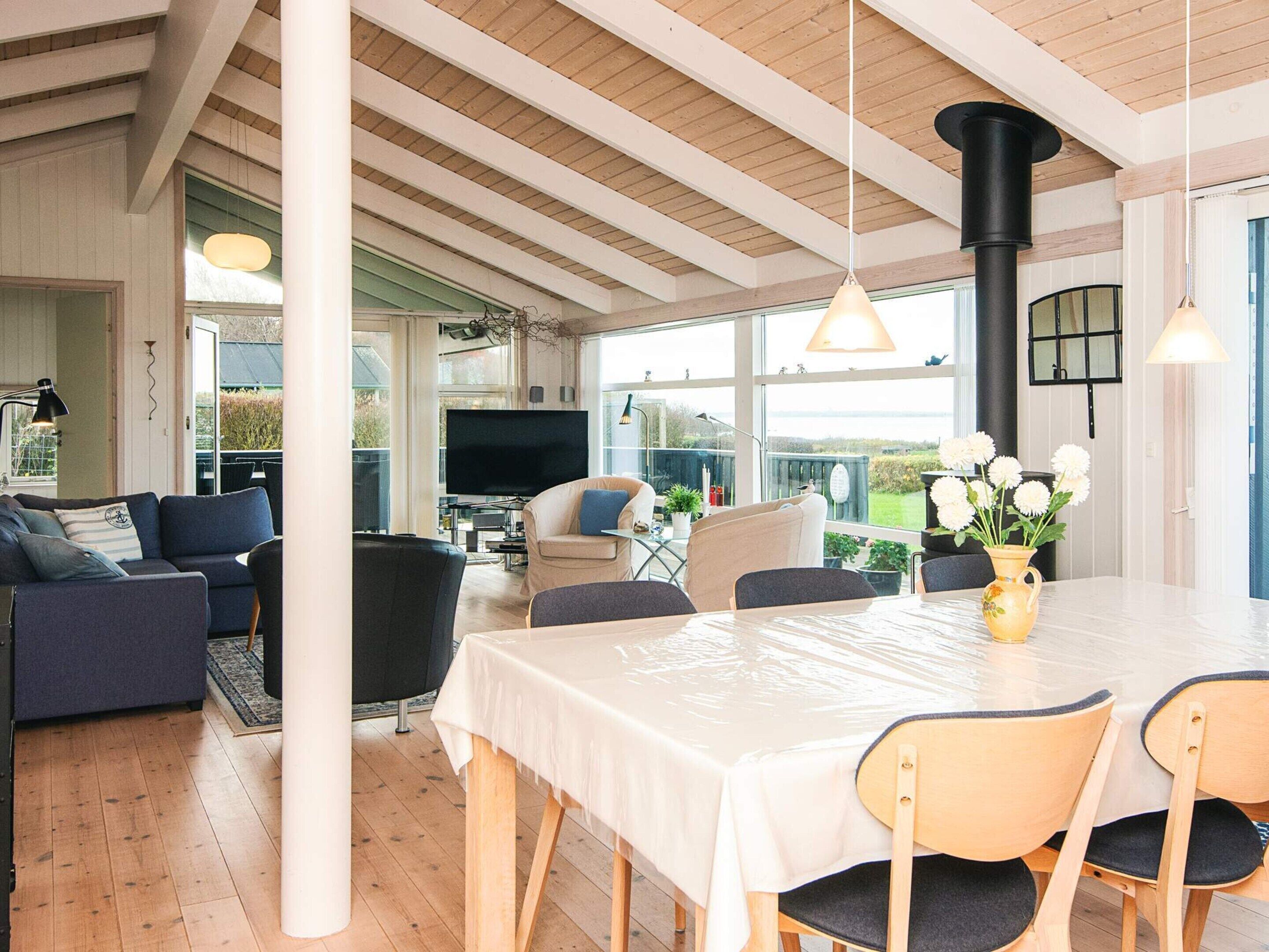 A spacious living area with a large window, a dining table, and a TV in the background.