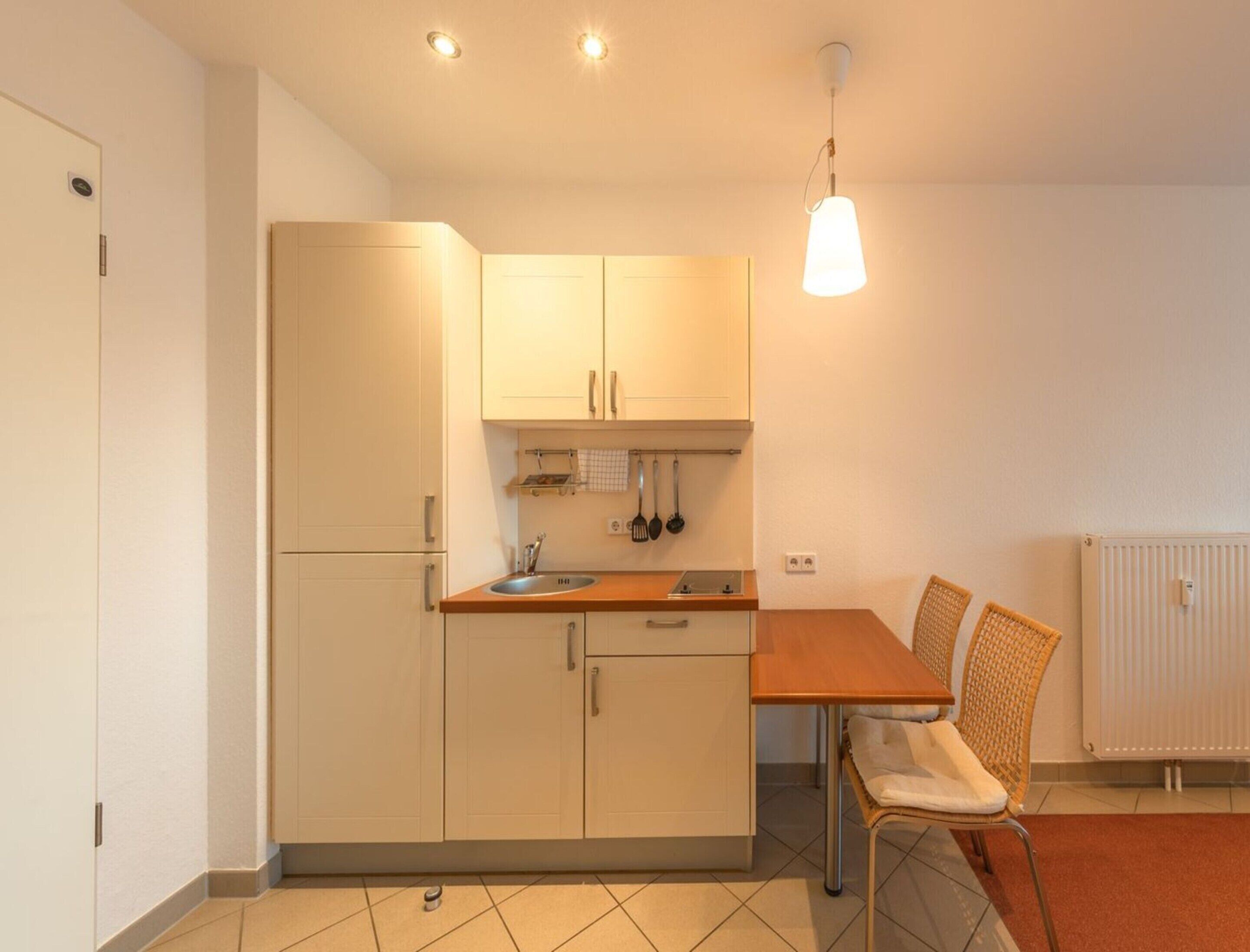 A compact kitchen with white cabinets, a wooden countertop, and a hanging light fixture.