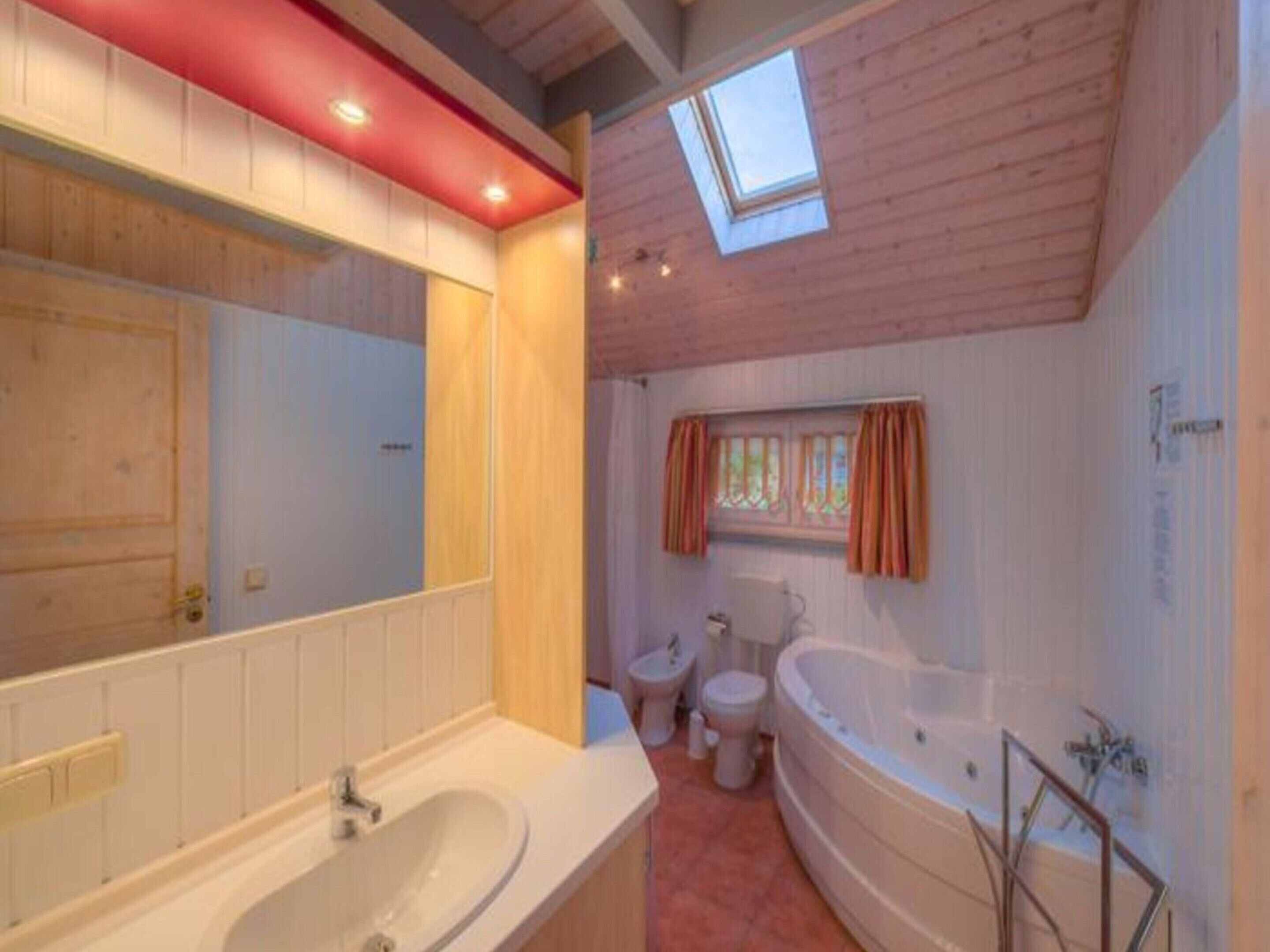 Une salle de bain avec un puits de lumière, une baignoire, des toilettes et un lavabo.