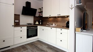 A modern kitchen with white cabinets, a built-in oven, and a wooden countertop. - Ferienhaus mit Garten (Dornum)