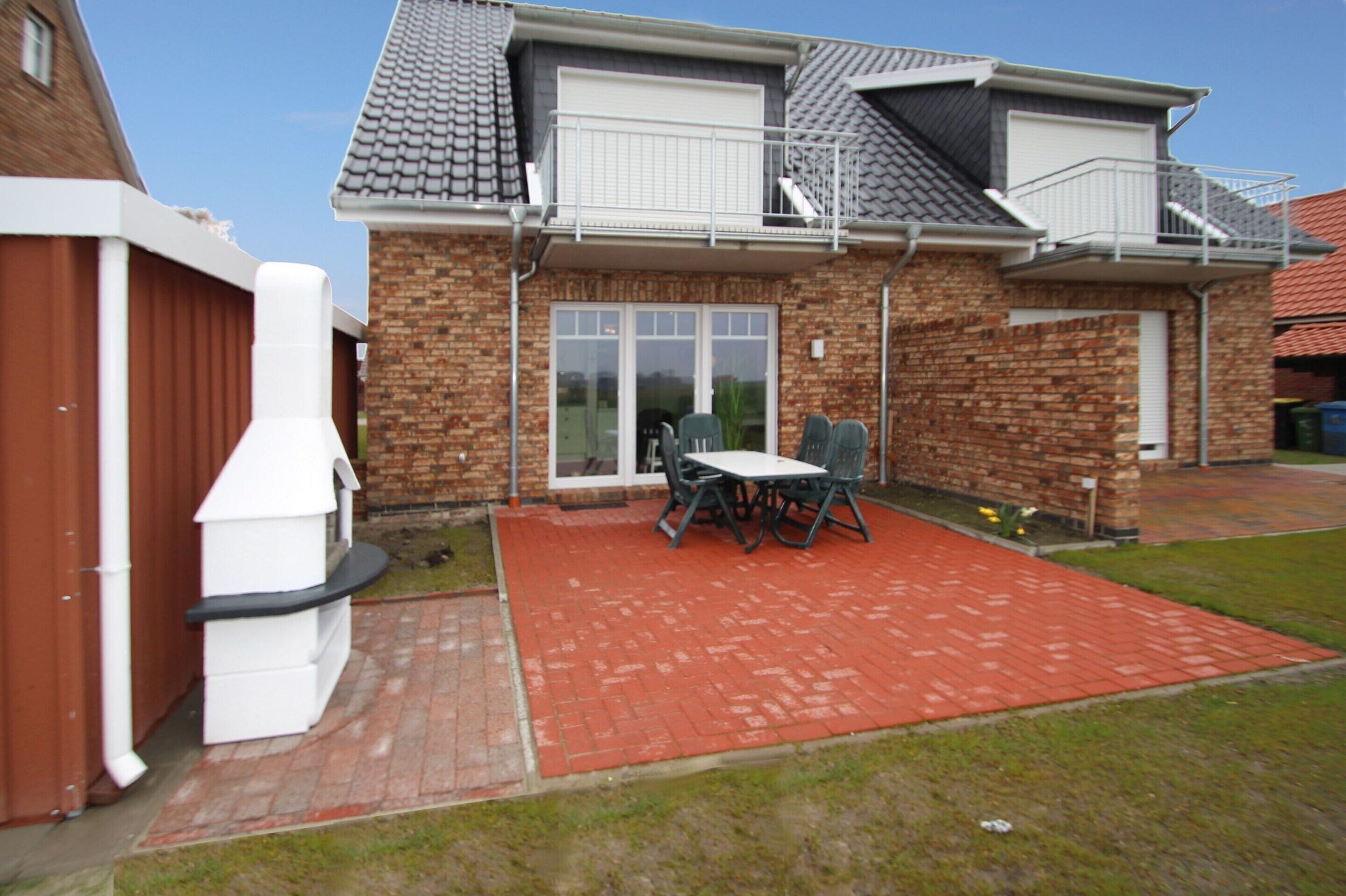 A two-story house with a brick exterior, a balcony, and a patio area with a table and chairs.