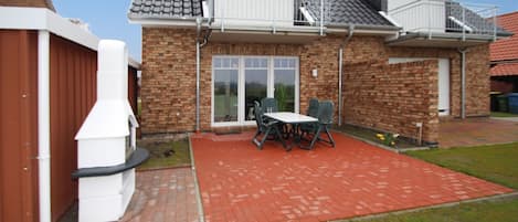 A two-story house with a brick exterior, a balcony, and a patio area with a table and chairs.