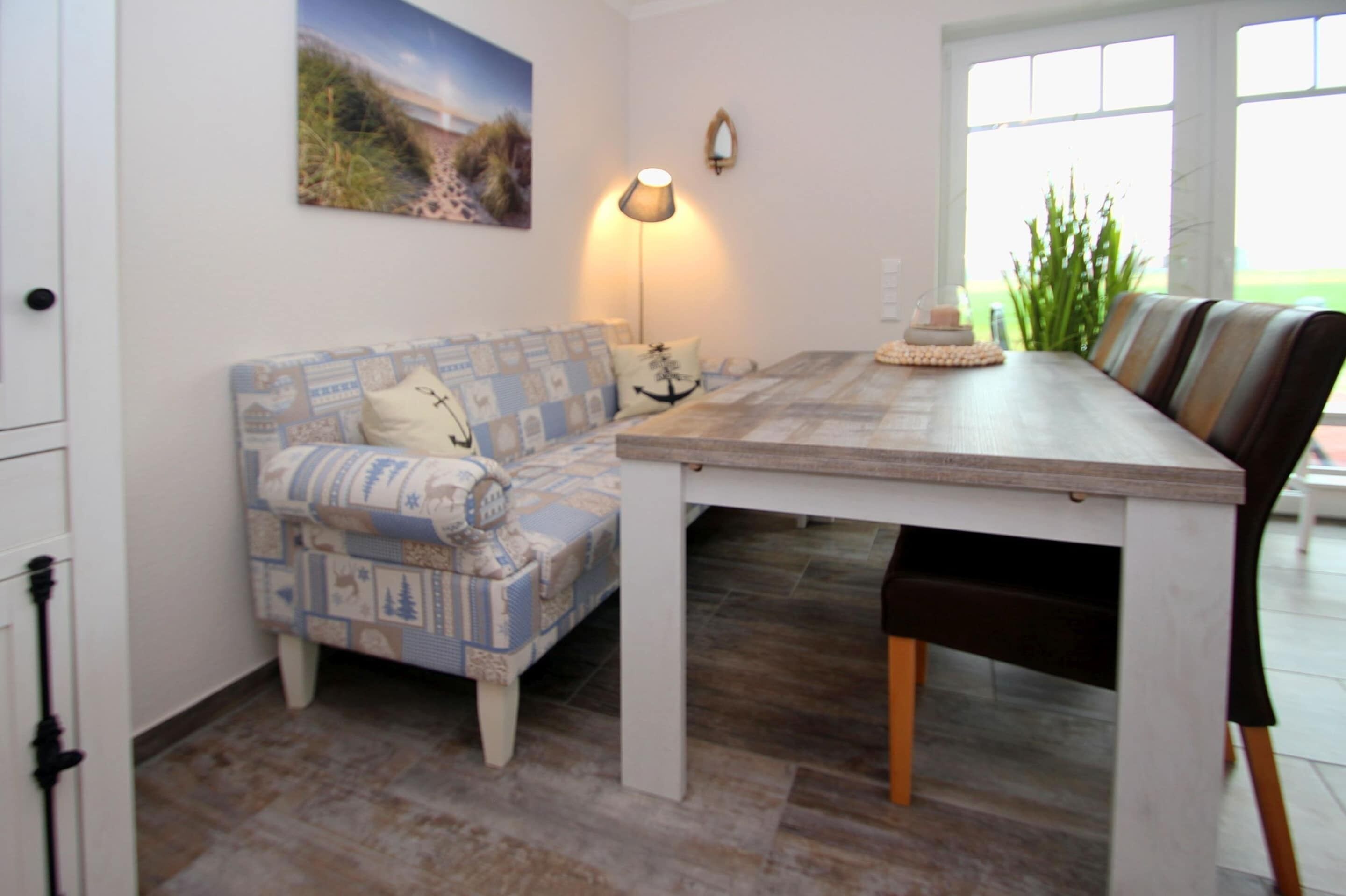 A dining area with a wooden table, a patterned sofa, and a lamp.