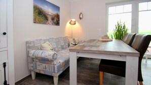 A dining area with a wooden table, a patterned sofa, and a lamp. - Ferienhaus mit Garten (Dornum)