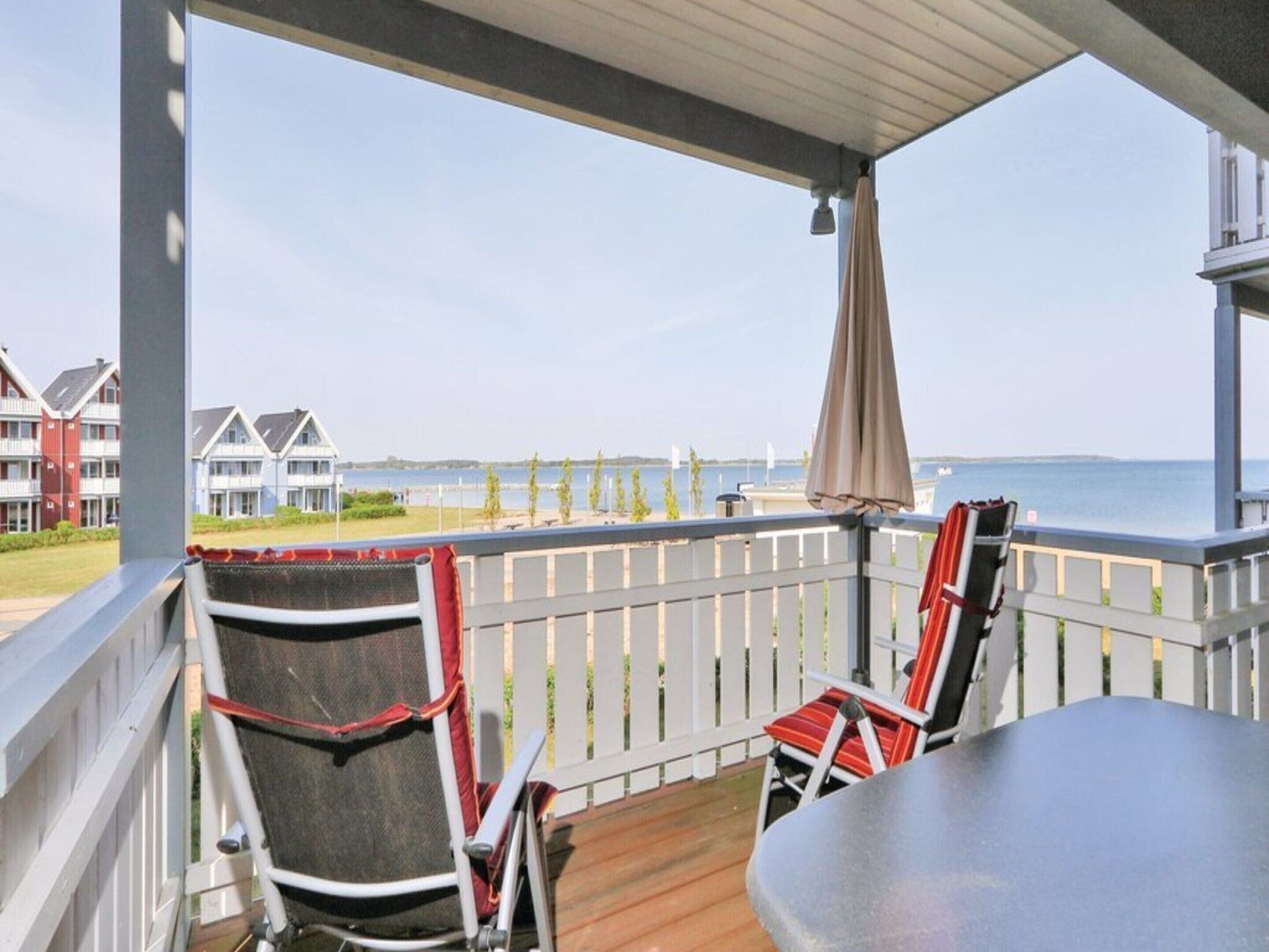Un balcon abrité, équipé de deux chaises et d’une table, qui offre une vue sur une plage et des bâtiments.