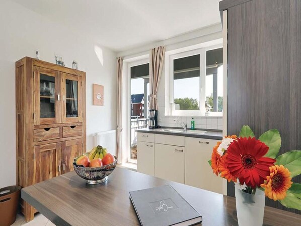 A kitchen with a wooden cabinet, a bowl of fruit, a laptop, and a vase with flowers.