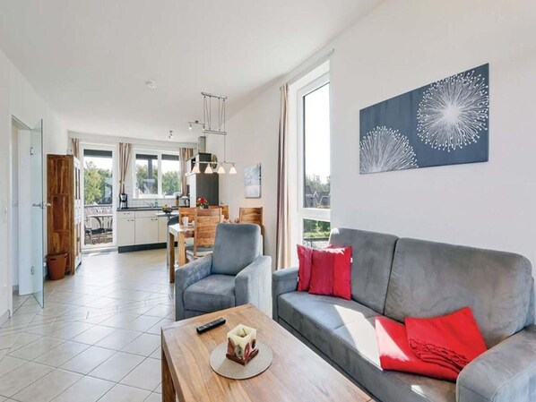 Ein modernes Wohnzimmer mit einem grauen Sofa, roten Kissen und einem Holztisch.