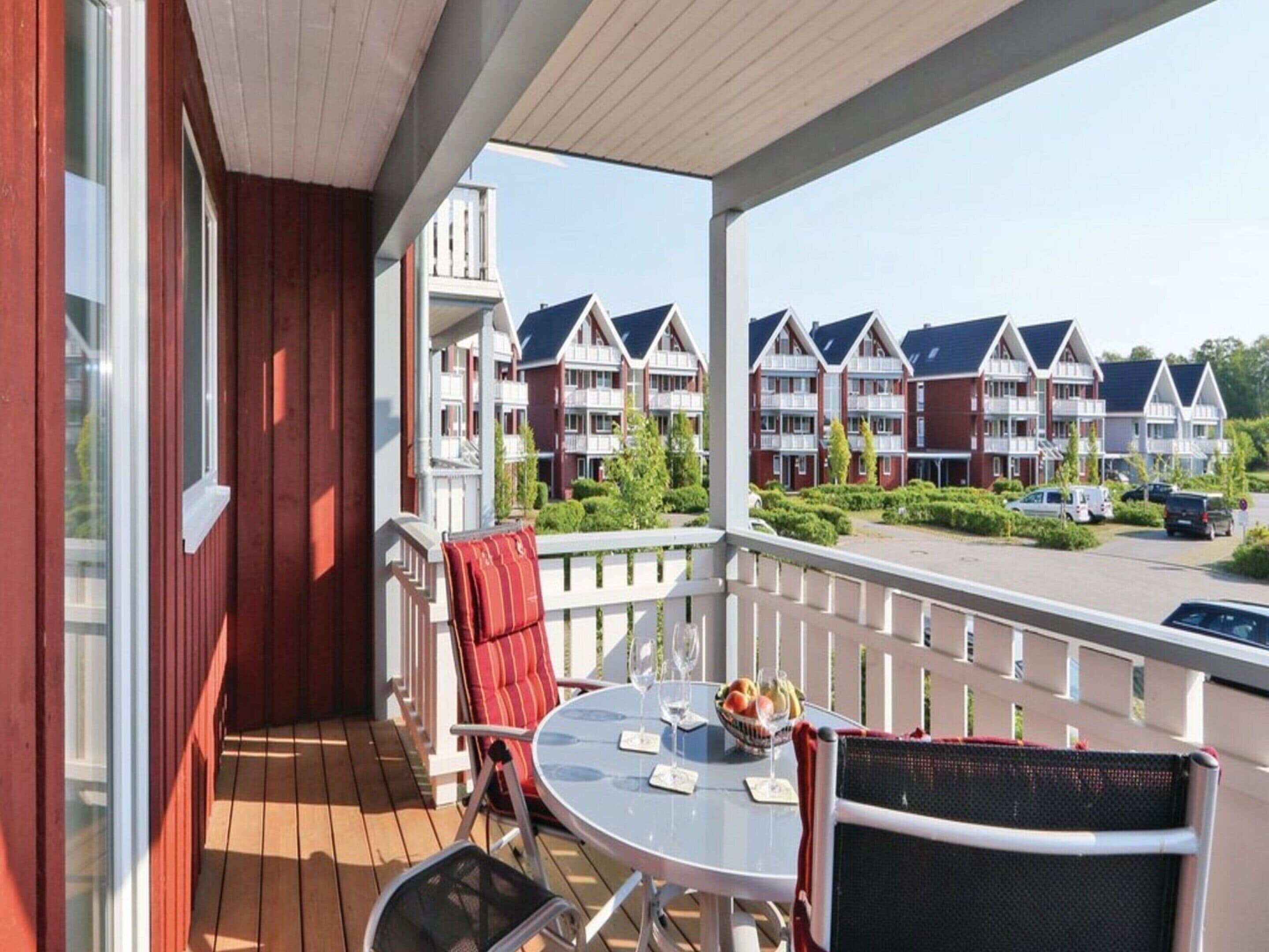 Un balcon avec une table ronde, des chaises et un coussin rouge.