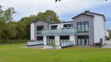 Une maison moderne à deux étages, dotée d’un balcon, de grandes fenêtres et d’une pelouse bien entretenue.