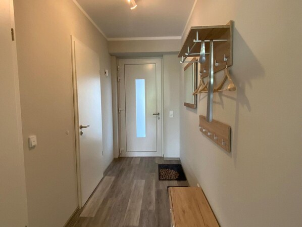 A narrow hallway with a wooden bench, a coat rack, and a door at the end. - Exclusives Appartement auf Fehmarn (Fehmarn)