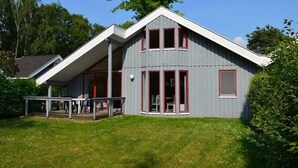 A two-story house with a grey exterior and red trim, featuring a covered patio area with a table and chairs. - Ferienhaus im Skandinavischen Stil (Mirow)