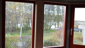 A room with two large windows offering a view of a wooded area and a grassy field. - Ferienhaus im Skandinavischen Stil (Mirow)