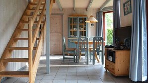 A room with a wooden staircase, a dining table with chairs, a cabinet with a television, and a window with curtains. - Ferienhaus im Skandinavischen Stil (Mirow)