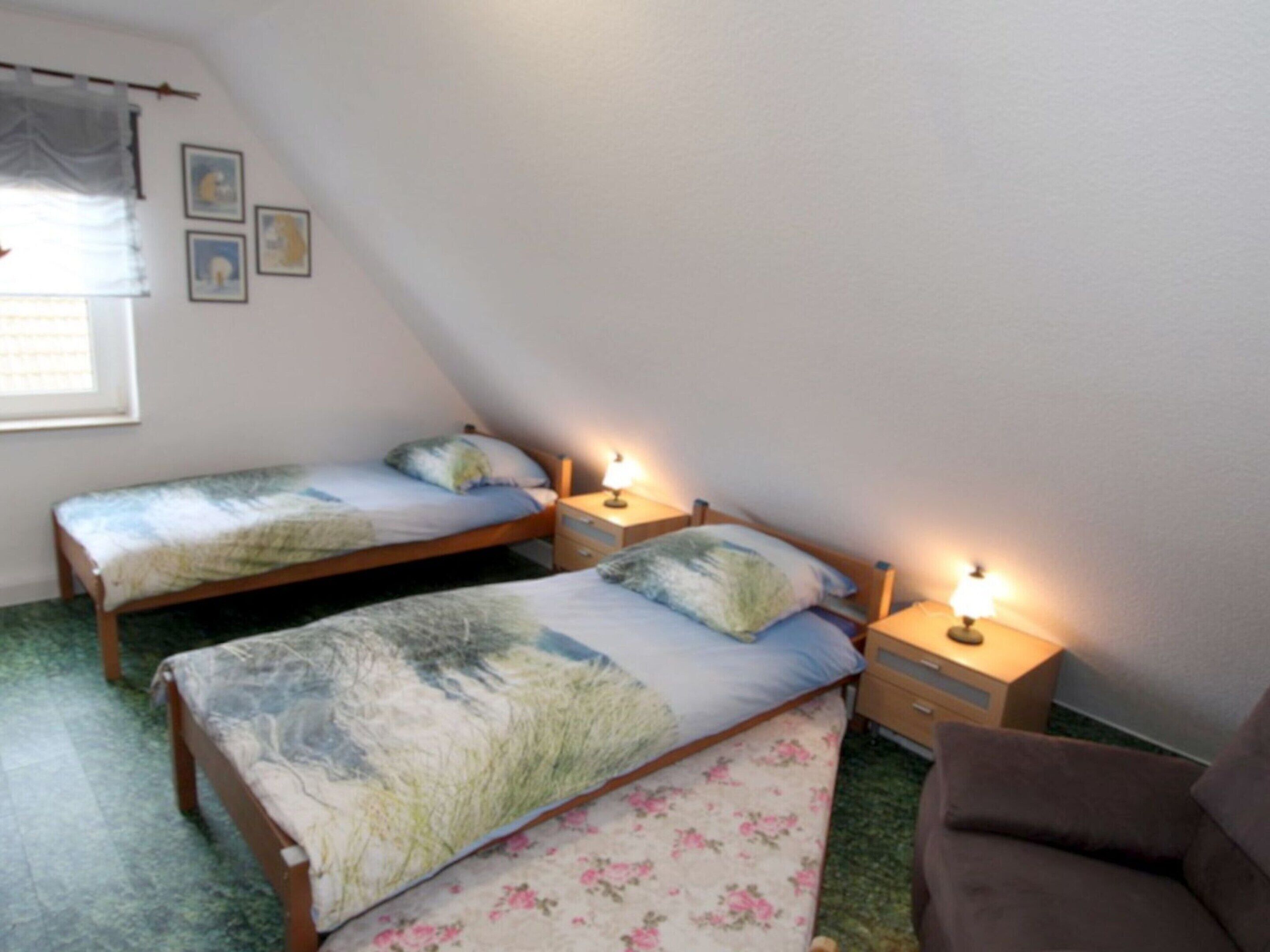 Una stanza accogliente e piccola con due letti singoli, ognuno dotato di comodino e lampada. La stanza presenta un soffitto spiovente e una finestra con persiane.