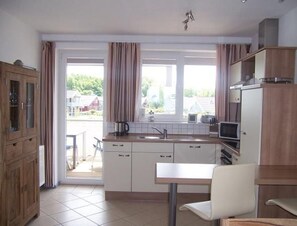 A modern kitchen with white cabinets, a dining table, and a view of the outside. - Exklusives Appartement in Rechlin (Rechlin)