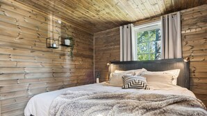 Een slaapkamer met houten lambrisering, een bed, een raam met gordijnen en een wandlamp.