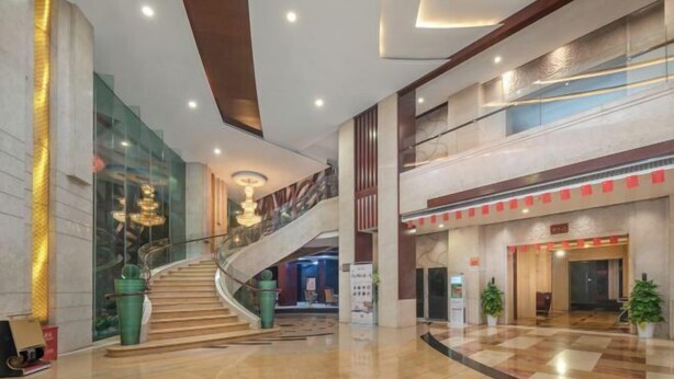 A spacious lobby with a marble floor, a central staircase, and a glass wall on one side.