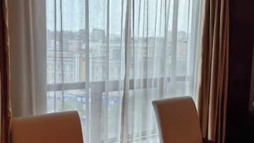 A room with two chairs facing a window with sheer curtains, offering a view of a cityscape.