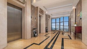 A modern hotel lobby with a marble floor, a large elevator, and a view through the glass doors.