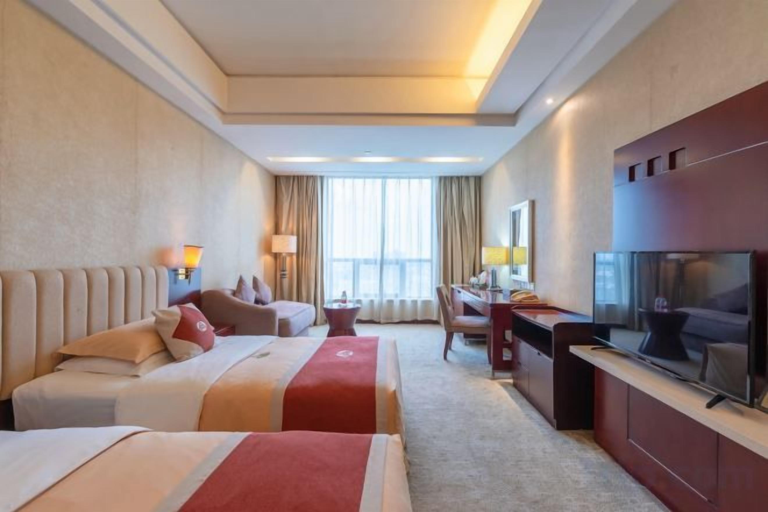 A hotel room with two beds, a desk, a television, and a large window.