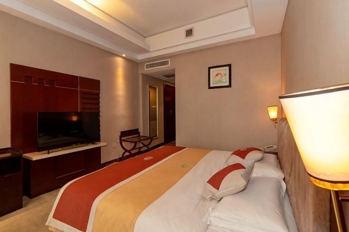 A hotel room with a bed, a TV, a desk, and a lamp.