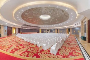Une grande salle de conférence avec un tapis rouge, des chaises blanches et une scène.