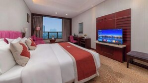 A hotel room with a large bed, a desk, a television, and a view of the city.