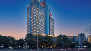 A high-rise hotel with multiple floors, a prominent vertical light strip, and a red logo on the top.