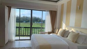Een slaapkamer met een groot bed, uitzicht op een grasveld door een schuifdeur, en een klein, rond tafeltje met een stoel.