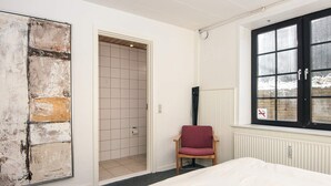 A bedroom with a large bed, a chair, a door leading to a bathroom, and a window with a view of the outside. - 6 Person Holiday Home in Give (Give)
