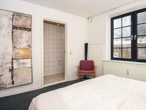 Une chambre avec un grand lit, une chaise, une porte donnant sur une salle de bain et une fenêtre avec vue sur l’extérieur.
