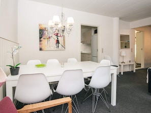 Un espace repas moderne avec une table et des chaises blanches, un lustre et un tableau au mur.