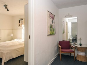 Une chambre d’hôtel avec un lit, une chaise, une petite table, un miroir et des œuvres d’art accrochées aux murs.