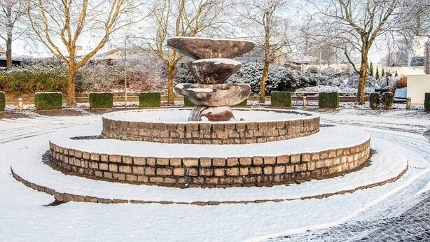 A snow-covered circular stone fountain with a tiered design, surrounded by a brick circular walkway. - 6 Person Holiday Home in Give (Give)