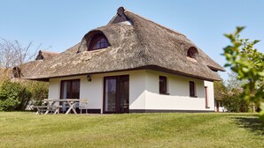 A house with a thatched roof, large windows, and a grassy lawn. - Ferienhaus im Van der Valk Resort in Linstow (Dobbin-Linstow)