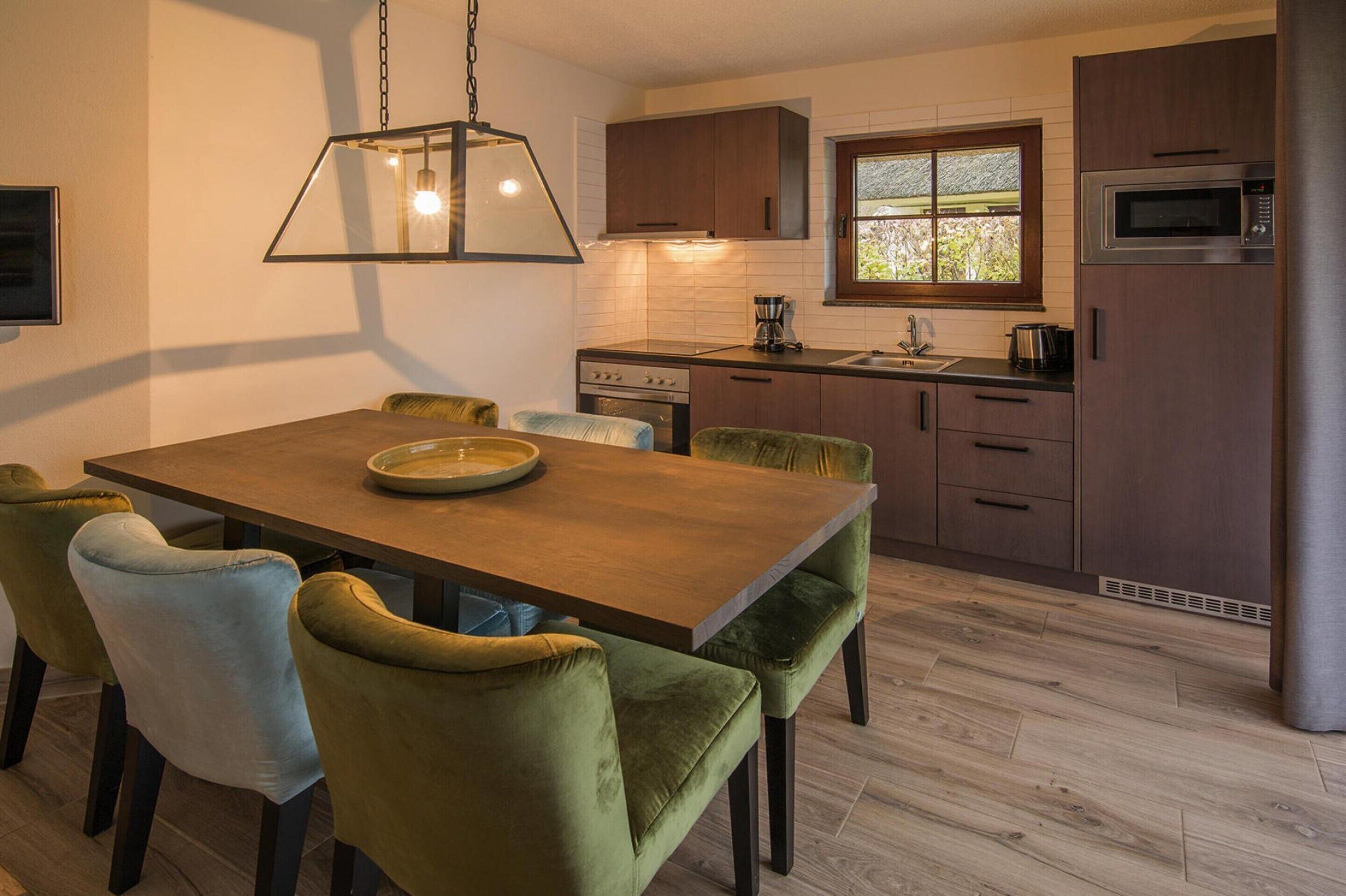 A modern kitchen with a wooden dining table, green upholstered chairs, a built-in oven, and a microwave.